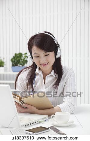 Stock Image - Woman reading book and listening music with smile. Fotosearch