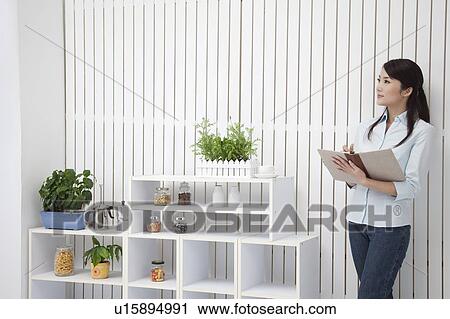 Stock Image - Woman standing, holding a notebook and looking away with smile. Fotosearch