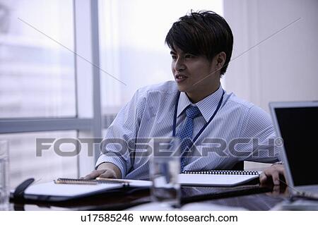 Stock Photograph - Young man sitting and looking away with smile in office. Fotosearch