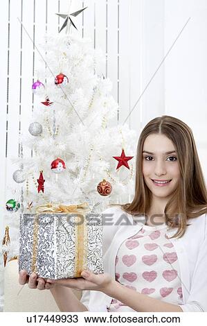 Young woman holding a gift and smiling at the camera View Large Photo Image Stock Image - Young woman holding a gift and smiling at the camera. Fotosearch