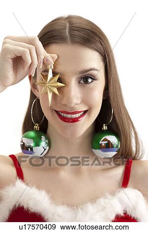 Young woman holding Christmas decoration on eye and smiling at the camera View Large Photo Image Stock Photo - Young woman holding Christmas decoration on eye and smiling at the camera. Fotosearch
