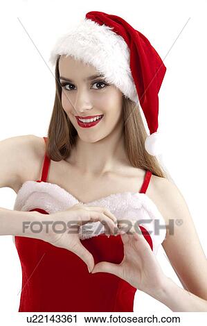 Stock Image - Young woman in Christmas clothing gesturing with heart shape and smiling. Fotosearch