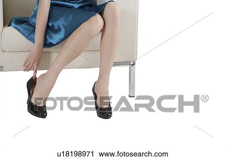 Stock Image - Young woman sitting on sofa and getting high heels on. Fotosearch