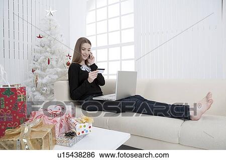 Young woman sitting on sofa, holding credit card and using laptop View Large Photo Image Stock Photograph - Young woman sitting on sofa, holding credit card and using laptop. Fotosearch