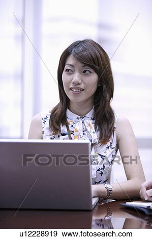 Stock Photo - Young woman using laptop and looking away. Fotosearch