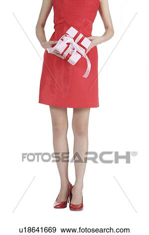 Stock Photo - Young woman wearing red dress and high heels and holding a gift. Fotosearch