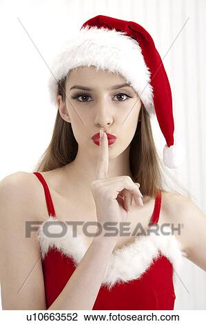 Stock Image - Young woman wearing Santa hat and putting finger on lips. Fotosearch