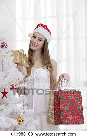 Stock Image - Young woman wearing Santa hat and holding shopping bags with smile. Fotosearch