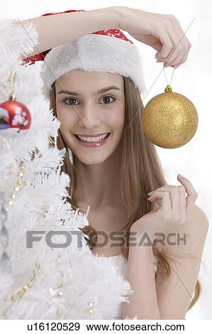 Young woman wearing Santa hat and holding a Christmas bauble with smile View Large Photo Image Stock Photo - Young woman wearing Santa hat and holding a Christmas bauble with smile. Fotosearch