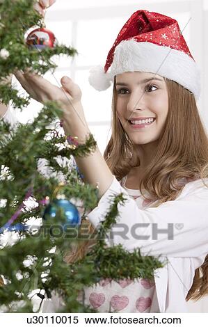 Stock Photography - Young woman wearing Santa hat and holding Christmas tree with smile. Fotosearch