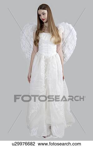 Stock Image - Young woman wearing white dress with wings and looking down. Fotosearch