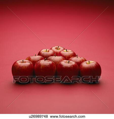 Stock Photo - Apples arranged in triangle, red background. Fotosearch
