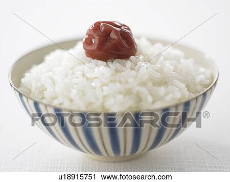 Stock Image - Bowl of rice with pickled plum, close up, white background. Fotosearch