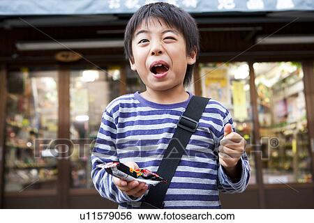 Boy holding a snack in his hand in front of Dagashi-ya View Large Photo Image Stock Photograph - Boy holding a snack in his hand in front of Dagashi-ya. Fotosearch