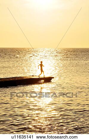 Stock Image - Boy playing at pier at dusk. Fotosearch