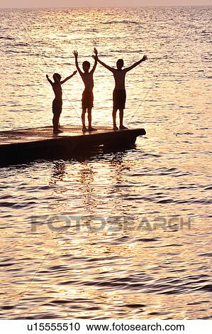 Stock Image - Boy playing at pier at dusk. Fotosearch