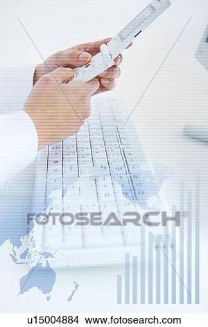 Picture - Businessman dialing a cell phone, world map and graph. Fotosearch