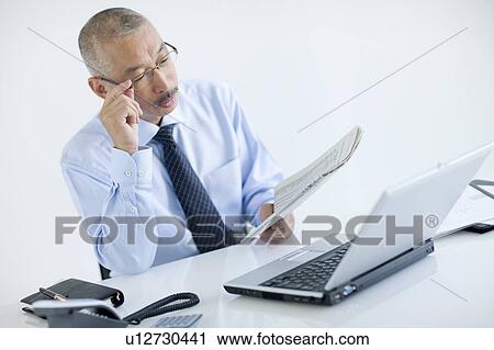 Stock Image - Businessman reading newspaper, white background. Fotosearch