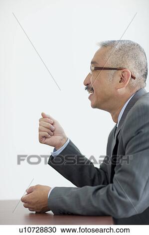 Stock Image - Businessman sitting at desk, white background. Fotosearch