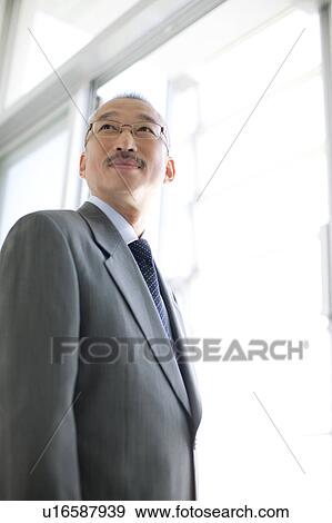 Stock Photo - Businessman standing by window, smiling and looking back. Fotosearch