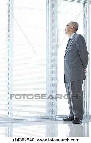 Stock Image - Businessman standing by window. Fotosearch