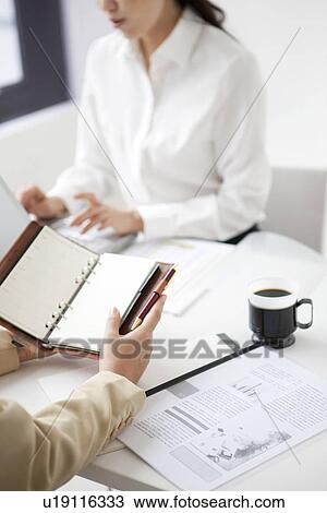 Businesswomen holding a diary and using laptop View Large Photo Image Stock Image - Businesswomen holding a diary and using laptop. Fotosearch