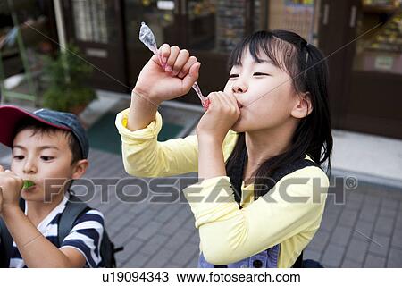 Stock Image - Children drinking juice in front of Dagashi-ya. Fotosearch