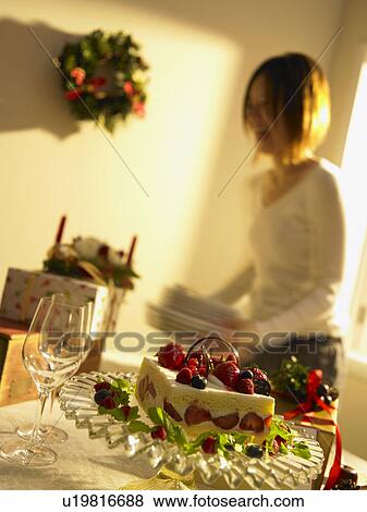 Stock Photo - Christmas cake on table, woman holding plates in background, blurred motion. Fotosearch