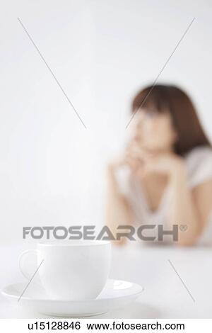 Stock Photograph - Cup and saucer, young woman in background, differential focus. Fotosearch