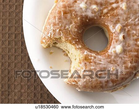 Stock Image - Doughnut with bite mark on plate, close up. Fotosearch