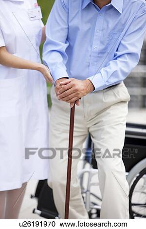 Stock Image - Female nurse helping man standing. Fotosearch