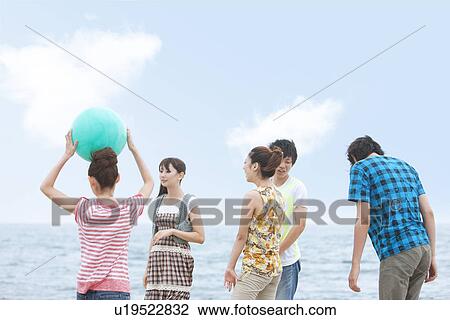 Stock Image - Five young people at beach, woman holding beach ball. Fotosearch