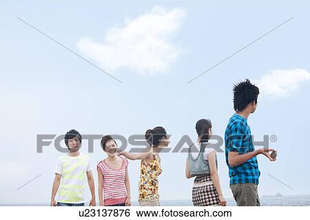 Stock Photograph - Five young people standing at beach. Fotosearch