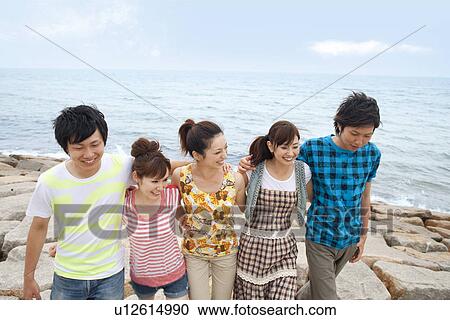 Stock Image - Five young people walking side by side at beach. Fotosearch