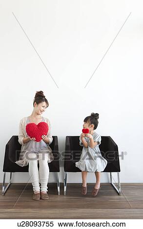 Stock Photography - Girl and woman holding red hearts on sofa, white background. Fotosearch