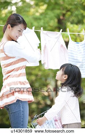 Stock Photo - Girl helping mother drying laundry, smiling. Fotosearch