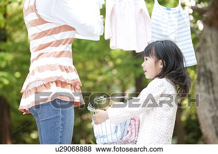 Stock Photo - Girl helping mother drying laundry, smiling. Fotosearch