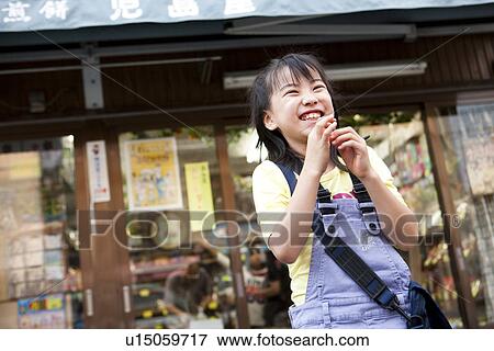Stock Photo - Girl in front of Dagashi-ya eating candy. Fotosearch