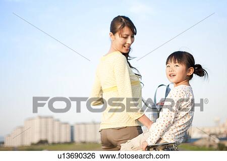 Stock Photograph - Girl with mother at riverbank, mother pushing bicycle. Fotosearch