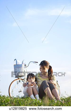Stock Photography - Girl with mother sitting at riverbank, playing harmonica. Fotosearch