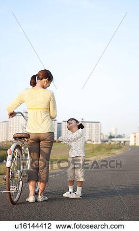 Stock Image - Girl with mother walking at riverbank, mother pushing bicycle. Fotosearch