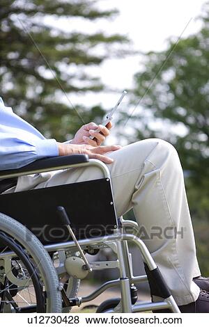 Stock Photo - Man in wheelchair using mobile phone. Fotosearch