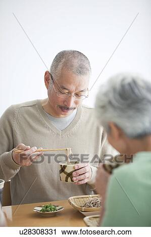 Stock Image - Mature couple eating soba noodles, white background. Fotosearch