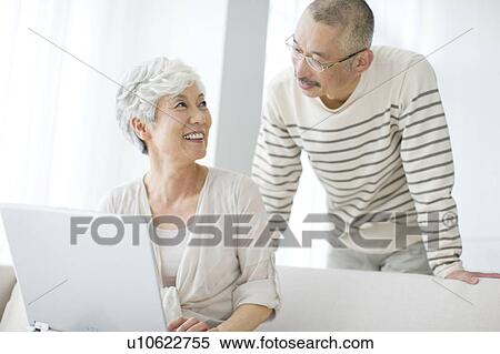 Stock Photography - Mature couple in living room, woman using laptop. Fotosearch