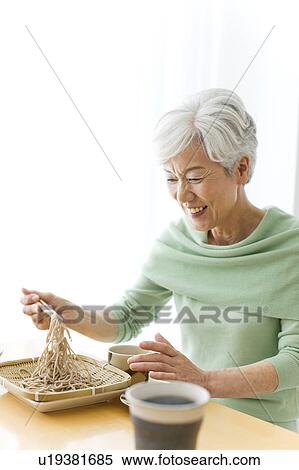 Stock Photography - Mature woman eating soba noodles, smiling. Fotosearch