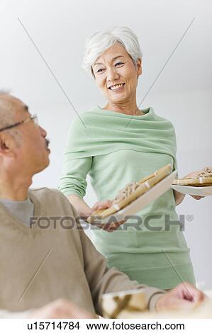 Picture - Mature woman holding soba noodles on colanders, white background. Fotosearch
