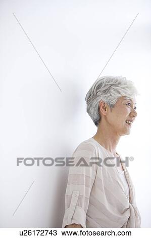 Stock Image - Mature woman smiling and looking away, white background. Fotosearch
