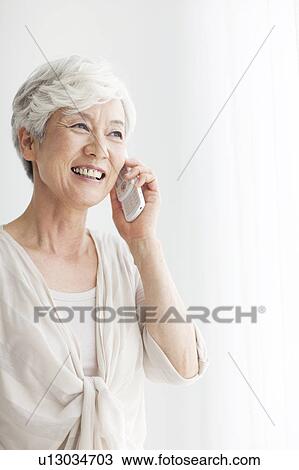 Stock Image - Mature woman using mobile phone, smiling, white background. Fotosearch
