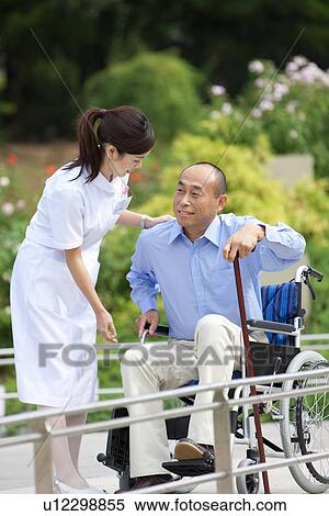 Stock Photography - Nurse assisting man with cane out of wheelchair. Fotosearch