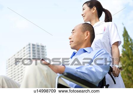 Stock Photo - Nurse pushing man on wheelchair. Fotosearch
